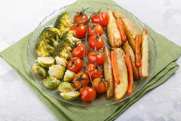 Oven baked vegetables with spices and herbs on a plate. Carrot, potato fries, tomatoes, brussel sprouts and broccoli.