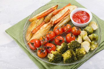 Oven baked vegetables with spices and herbs on a plate. Carrot, potato fries, tomatoes, brussel sprouts and broccoli served with tomato sauce.