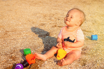 Happy baby sitting on a beach and enjoying morning sun light. Child playing with sand shapes and having fun. Happy childhood and enjoying the moment concept