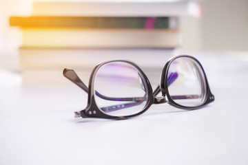 Stylish black glasses on a white background and blurred books.