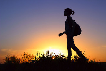 People, Teens, Hiking and Travel Concept. Silhouette Of A Young Girl On A Mountain Top.Young Girl With Backpack Enjoying Sunset.Tourist Traveler At Sunset.
