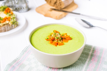 Bowl of Green peas cream soup with baked carrot and microgreen sprouts on the served white wooden table. Healthy food, vegitarian diet concept. Selective focus, space for text.
