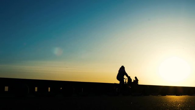 Silhouettes of cyclists riding in the park, women with a stroller walking at sunset