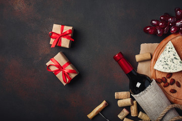 Bottle of wine, gift box, red grapes, almonds, corkscrew and corks, on rusty background top view