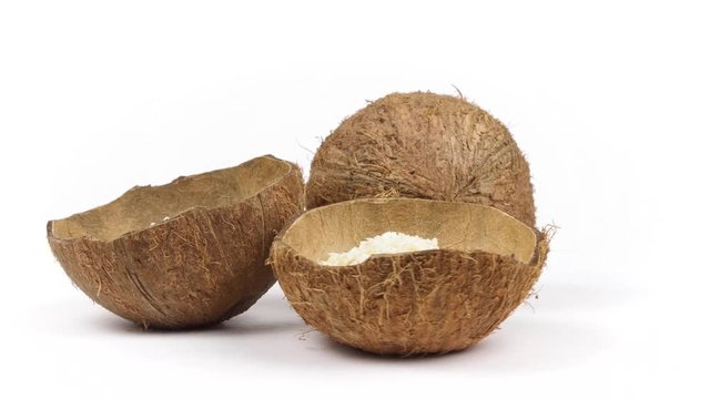 One whole and two shells halves of tropical coconut with dried white coconut flakes rotating on white isolated background. Healthy tropical fruits. Loopable seamless cocos rotating
