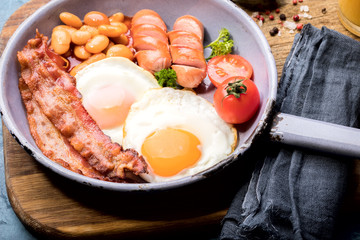 Traditional English Breakfast in the Frying Pan  Food on the Blue Background. Eggs, Sausages, Bacon, Beans,Toasts,Coffe and Orange juice