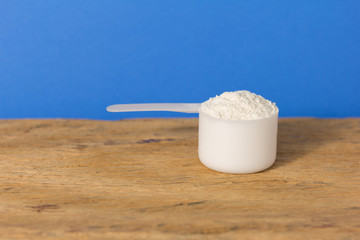 Whey Protein. Close up of scoop filled with vanilla flavour powder over wood table. Color background: blue.