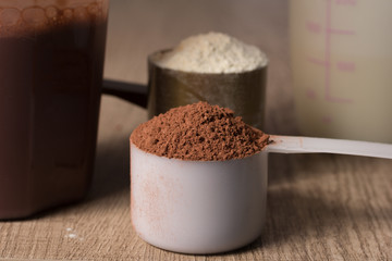 Whey Protein. Two scoops with vanilla and chocolate flavour powder, shaker. Wooden table. Close up, texture.