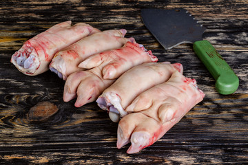 Raw and freesh pork feet or legs,over dark wooden board. They are stacked pile. With a cutting ax. Food meat shot.