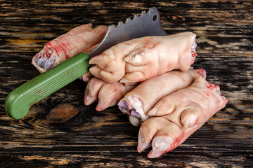 Raw and freesh pork feet or legs,over dark wooden board. They are stacked pile. With a cutting ax. Food meat shot.