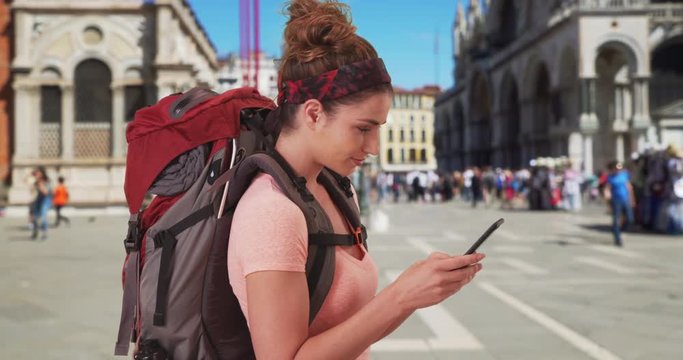 Vacationing white female backpacker checking mobile device at St, Mark's Square