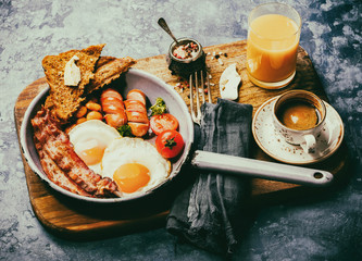 Traditional English Breakfast in the Frying Pan  Food on the Blue Background. Eggs, Sausages, Bacon, Beans,Toasts,Coffe and Orange juice Toned image Vintage style