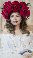 Girl model posing. a young woman in a wreath of scarlet peonies on her head, dark long curly hair descends on small shoulders