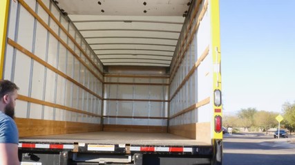 Wide shot of a man pushing in a metal ramp on a moving truck in 4k. The young mover puts the loading ramp away into the back of the rental van. Shot represents relocating for work and a fresh start.