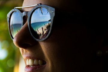 Reflection of the beach on sunglasses of a smiling girl in Koh Pha Ngan, Thailand. Summer travel vacation, accessories concept. Fashion model