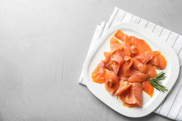 Plate with fresh sliced salmon fillet and rosemary on gray background, top view