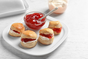 Tasty scones with clotted cream and jam on light background