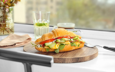 Tasty croissant sandwich with salami on window sill