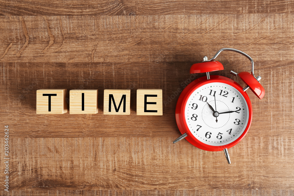 Aufkleber cubes with text time and alarm clock on wooden background, top view