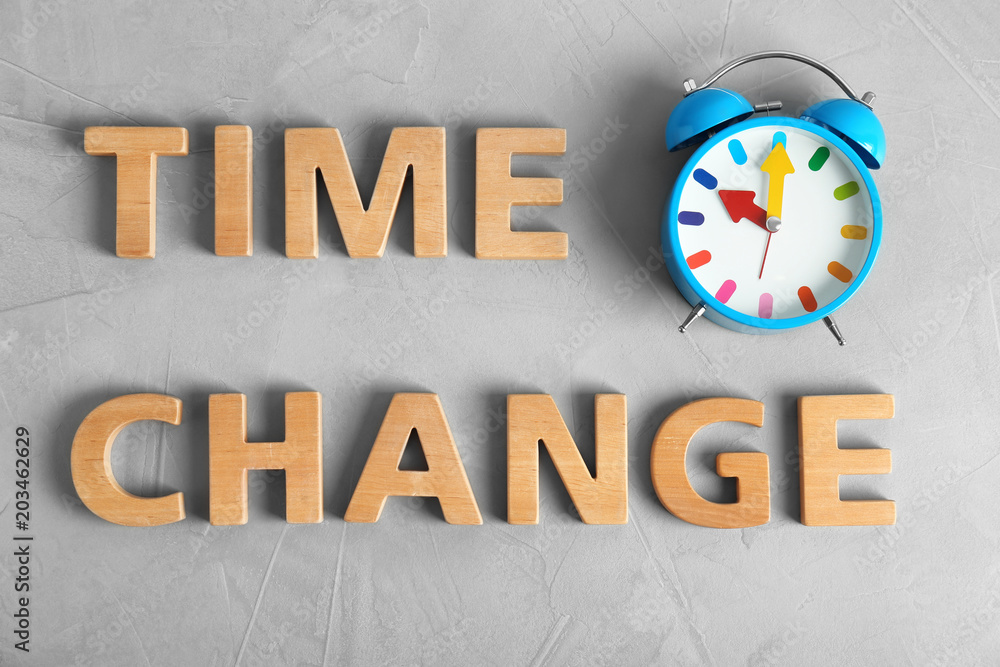 Poster Text TIME CHANGE made of letters and alarm clock on table