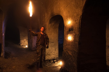 Man with torch explores ancient abandoned underground temple. 