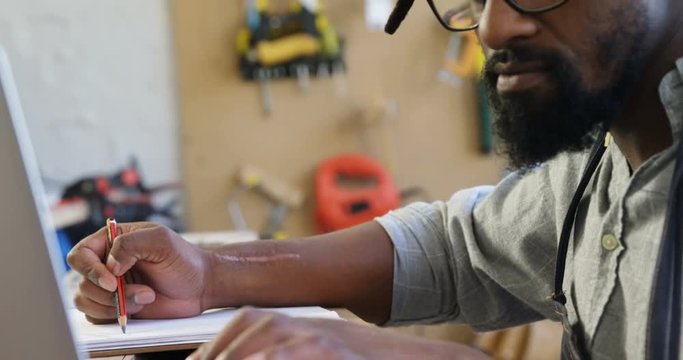 Carpenter writing in notepad while using computer 