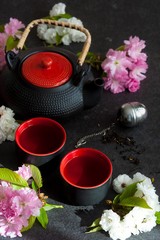 Tea concept, cups with tea and traditional teapot decorated with blooming spring tree branch 