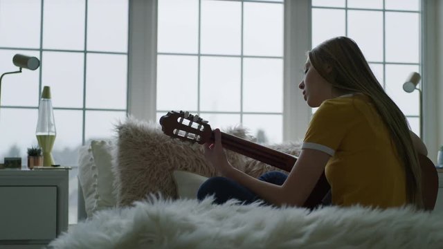 Girl sitting on bed playing guitar and singing / Highland, Utah, United States