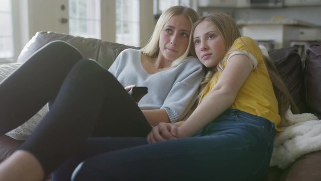 Serious sisters cuddling on sofa and watching television / Highland, Utah, United States