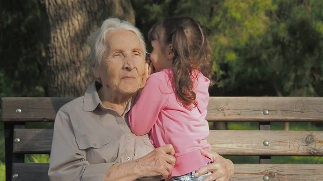 Elderly woman with a child in the park. Grandmother and granddaughter are talking in nature.