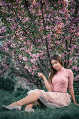 a girl in a pink dress stands smiling near the cherry blossom