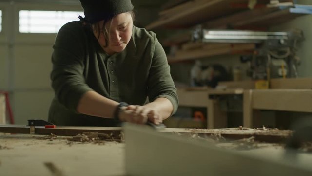 Slow motion tilt up to woman sanding wood plank in workshop / Provo, Utah, United States