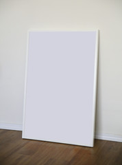 Blank poster in a white frame on the wood floor