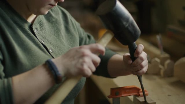Slow motion tilt down on woman chiseling wood in workshop / Provo, Utah, United States