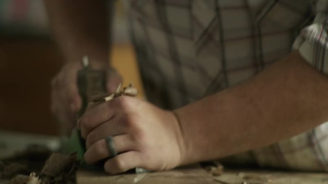 Slow motion tilt up of man shaving wood in workshop using hand plane / Provo, Utah, United States