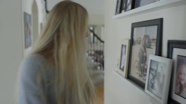 Tracking shot of girl descending staircase then kissing photograph in corridor / Highland, Utah, United States