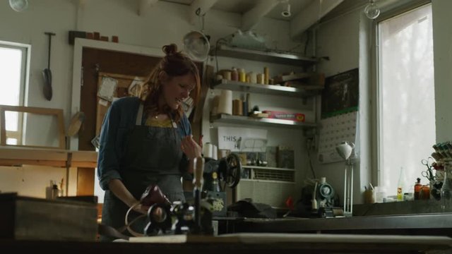 Woman repairing shoe in workshop hurting thumb / Provo, Utah, United States