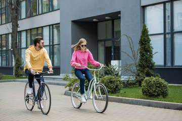 young stylish couple in sunglasses riding on bicycles
