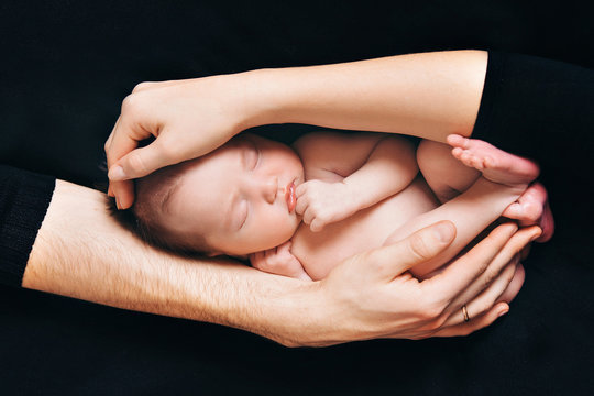 newborn baby lying on the parent's on a black background. Imitation of a child in the womb. beautiful little girl sleeping lying on her side. The baby raised his hand to his mouth