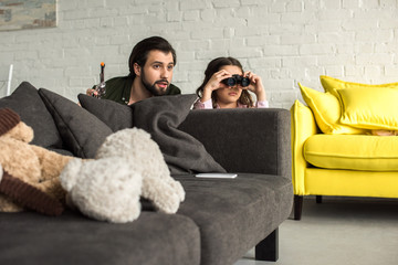 Naklejka premium father and daughter playing with toy gun and binoculars at home