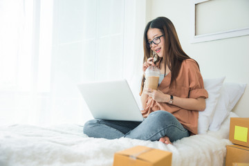 Fototapeta na wymiar Beauty Asian woman using laptop and drinking coffee on bed. Business and Technology concept. Delivery and Online shopping concept. Post and Service theme.