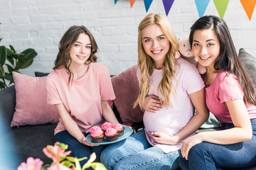 multicultural friends and pregnant woman with pink cupcakes at baby shower party