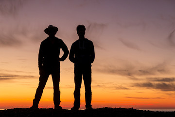 The silhouette of two young men turning back to a beautiful sunset.
