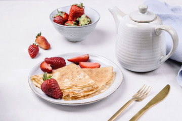 Openwork thin cheese crepes served with strawberry on grey concrete background. Homemade pancakes. Delicious breakfast
