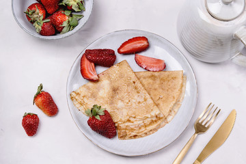 Openwork thin cheese crepes served with strawberry on grey concrete background. Homemade pancakes. Delicious breakfast