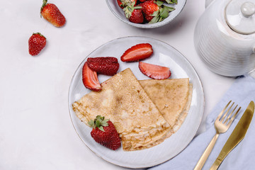 Openwork thin cheese crepes served with strawberry on grey concrete background. Homemade pancakes. Delicious breakfast