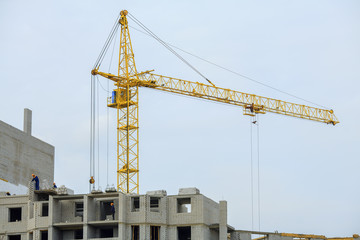 Yellow crane and building under construction against blue sky.