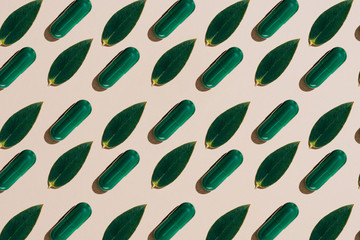 top view of phytotherapy capsules with green leaves in rows pattern on beige tabletop