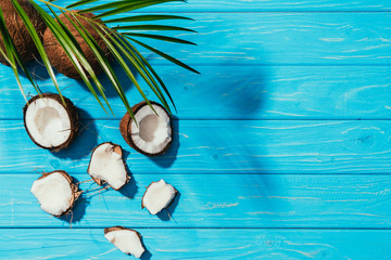 top view of coconuts and green palm leaves on turquoise wooden surface