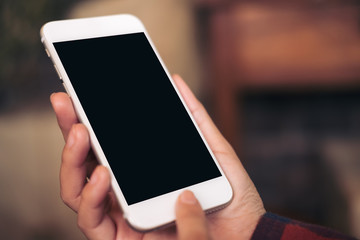 Mockup image of hands holding and using white mobile phone with blank black screen in cafe